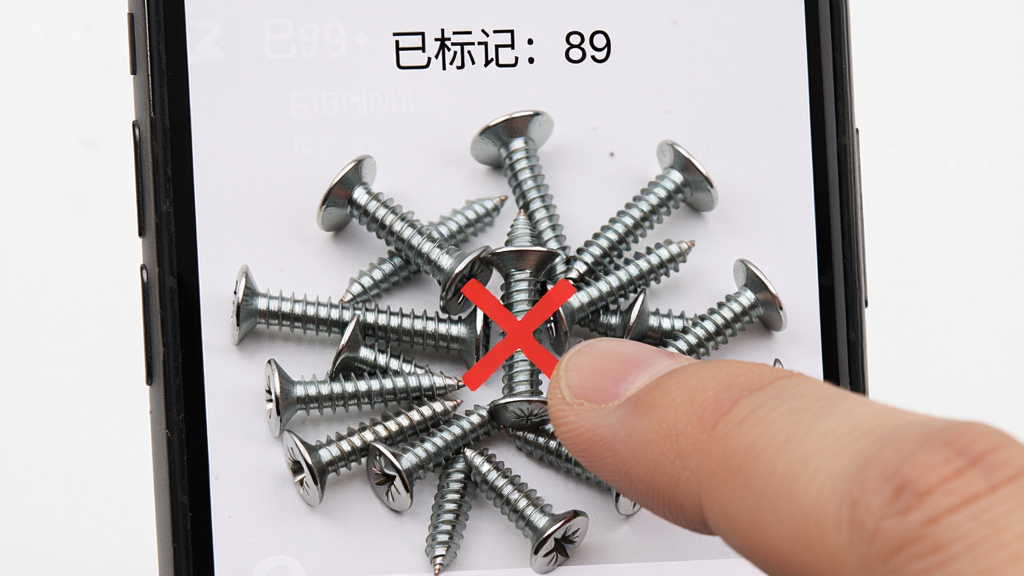 拍照扫描计数手动修正功能演示图,画面展示手机屏幕上一堆螺丝钉,其中一个螺丝钉上有一个红色的叉号,用户手指正点击另一个未标记的螺丝钉,屏幕上方显示“已标记:89”。主体是手机和手指操作,布局为竖屏特写,风格为工具类应用操作演示,细节有螺丝钉的金属质感和红色标记,画质清晰,干净,无多余元素