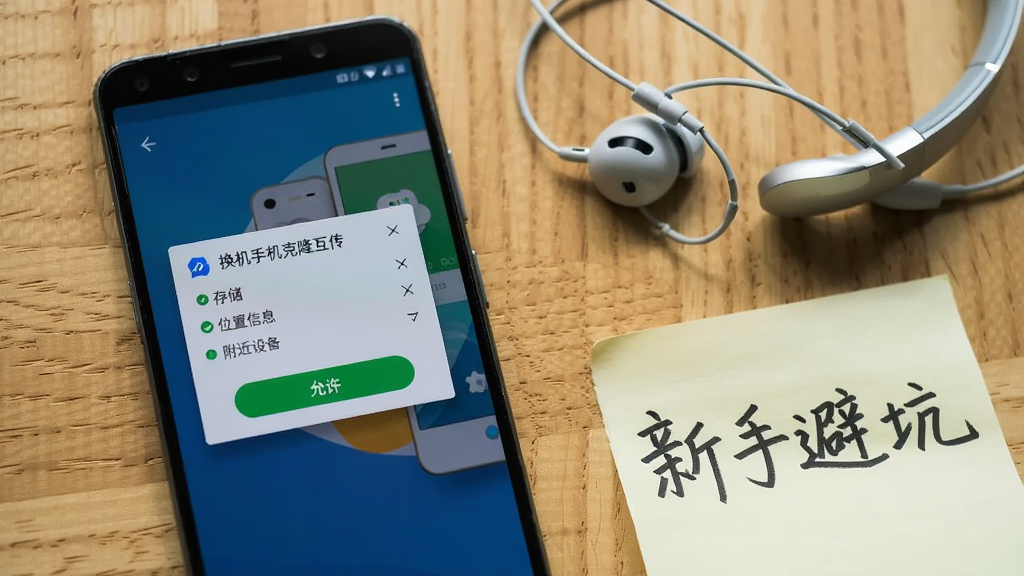 一部安卓手机屏幕显示“换机手机克隆互传”软件的权限授权弹窗界面,弹窗中列出存储、位置信息、附近设备三项权限并带有允许按钮,手机旁边放着一副耳机和一张写着“新手避坑”的便签纸,背景为木质桌面,风格生活化写实,光线自然,画面干净,高清画质