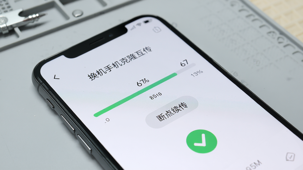 一部手机屏幕上显示“换机手机克隆互传”的传输进度界面,进度条显示百分之六十七,旁边有“断点续传”按钮和绿色对勾校验图标,背景为浅灰色工作台面,画面风格写实清晰,光线柔和,重点突出软件界面细节,高清画质,无多余杂物