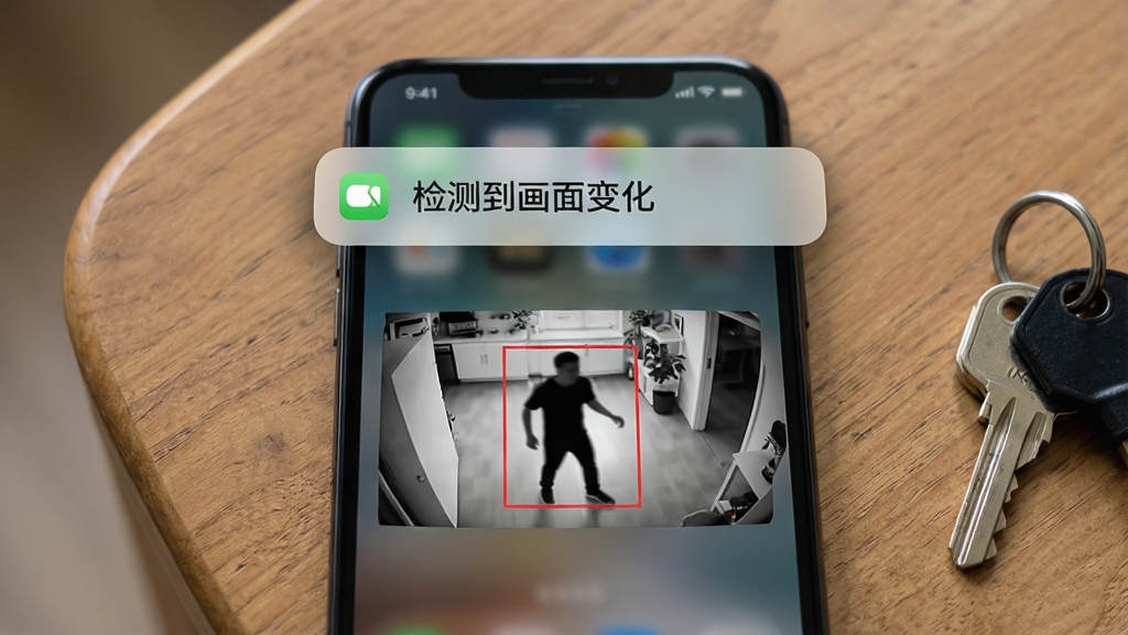 一部手机屏幕弹出通知横幅,横幅上写着“检测到画面变化”,横幅下方是监控画面缩略图,画面中有一个移动的人影轮廓被红色方框标注。手机放在木质桌面上,旁边有一串钥匙。布局为手机居中、通知横幅位于屏幕上方三分之一处。风格为写实UI展示风,细节上强调通知横幅的圆角与阴影质感,画质高清、干净、无多余元素。