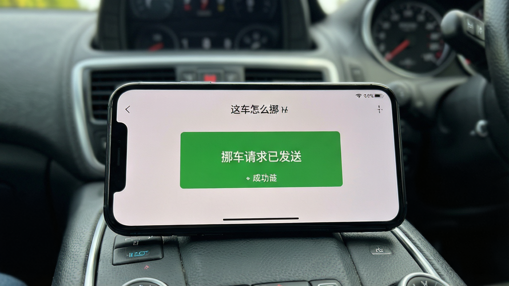 主体为「这车怎么挪」应用在手机上的实际运行效果,屏幕显示“挪车请求已发送”的绿色成功提示页面。手机横放在驾驶室中控台上,背景为模糊的车内环境。布局为第一视角拍摄风格。风格写实,光线自然,细节展示清晰,画质干净,无多余元素。