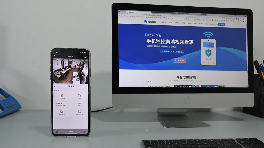 一部手机和一台电脑并排放在桌面上,手机屏幕显示监控画面和设置菜单,电脑屏幕显示官方网站下载页面,画面中有“手机监控高清视频看家”的文字,背景为简洁的浅灰色工作台,布局采用左右并列式,风格写实,强调查看教程与安装步骤,画质干净无多余元素。