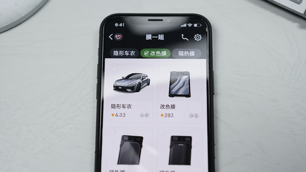�������ֻ���Ļ��д����Ļ����ʾ��Ĥһ�㡱APP�Ĳ�Ʒ�б����棬�����ڰ������γ��¡���ɫĤ������Ĥ�ȷ����ǩ�Ͳ�Ʒ��Ƭ������Ϊ�ֻ����С�����Ϊǳ��ɫ���棬�Ű�������湹ͼ�����Ϊ�����Ʒչʾ�磬ϸ�ڰ�����Ļ������Ȼ������ͼ�������ɱ桢��Ʒ����ͼɫ����ʵ������Ϊ���塢�ɾ����޶���Ԫ��