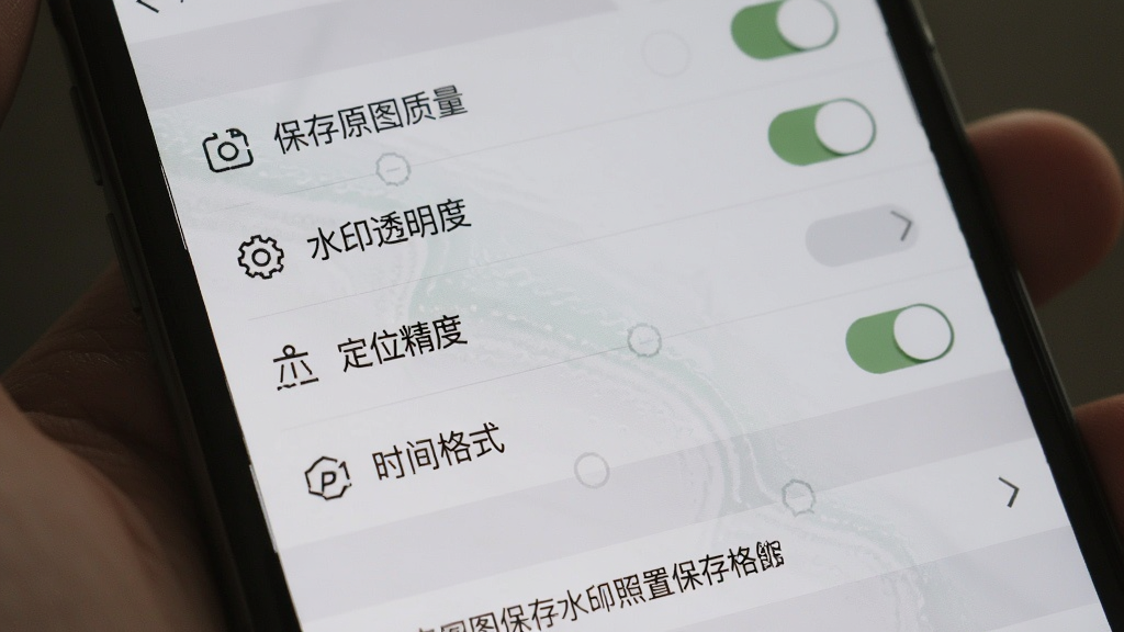 一张展示炅图水印相机照片保存设置界面的图片,画面中手机屏幕显示设置菜单,菜单项包括保存原图质量、水印透明度、定位精度、时间格式等选项,界面底部有保存路径显示,整体布局简洁,采用浅灰质感风格,细节包括开关按钮的样式、选项图标的线条,画质清晰,干净,无多余元素