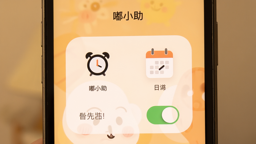 手机屏幕显示“嘟小助”提醒设置界面,界面上有闹钟图标、日历图标和开关按钮,背景为柔和暖色调。布局为居中展示,风格为温馨实用风,细节清晰,画质干净,无多余元素。